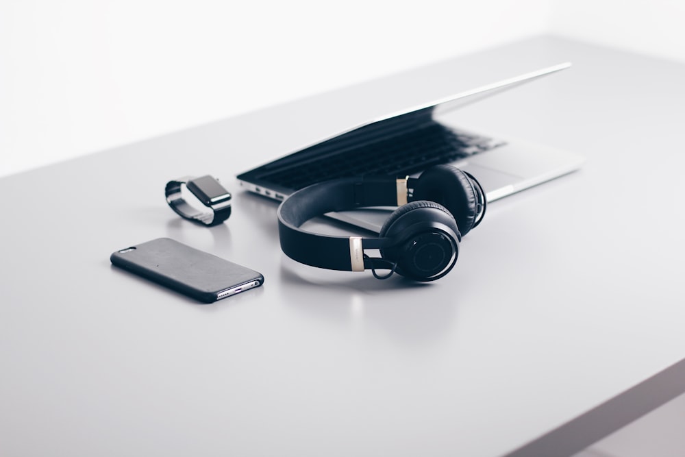 black cordless headphones beside closed black laptop computer and smartphone