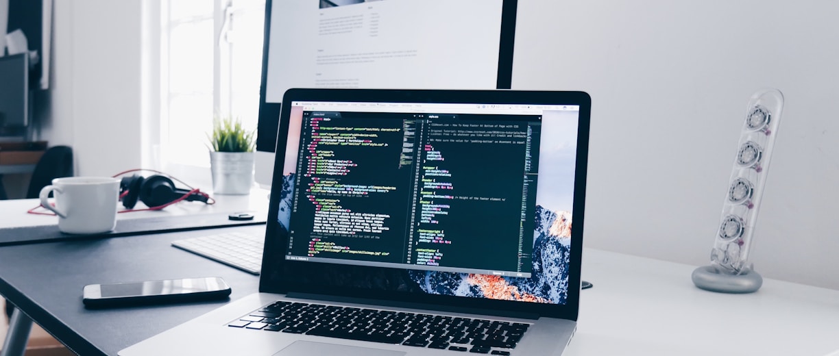 A MacBook with lines of code on its screen on a busy desk