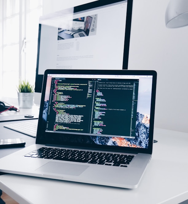 A MacBook with lines of code on its screen on a busy desk