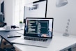 A MacBook with lines of code on its screen on a busy desk
