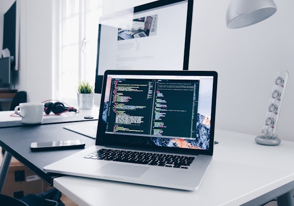 A MacBook with lines of code on its screen on a busy desk