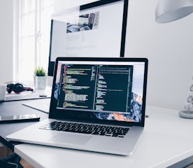 A MacBook with lines of code on its screen on a busy desk