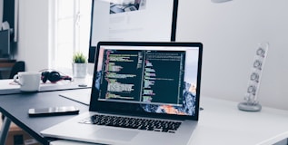 A MacBook with lines of code on its screen on a busy desk