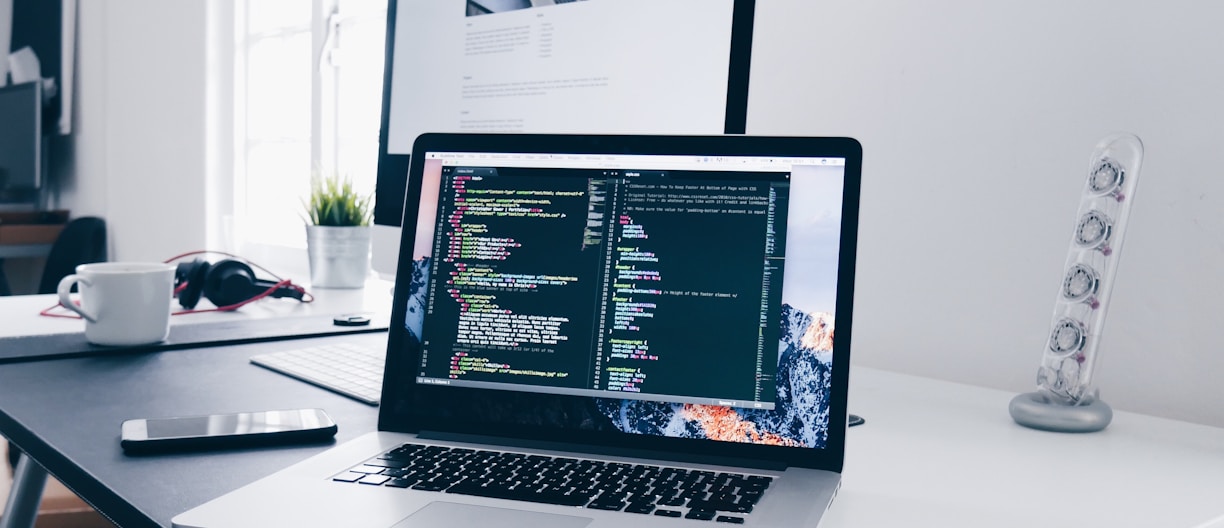 A MacBook with lines of code on its screen on a busy desk