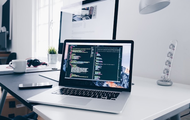 A MacBook with lines of code on its screen on a busy desk