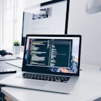 A MacBook with lines of code on its screen on a busy desk