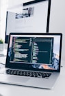 A MacBook with lines of code on its screen on a busy desk