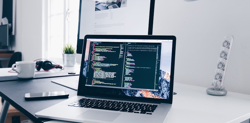 A MacBook with lines of code on its screen on a busy desk