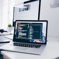 A MacBook with lines of code on its screen on a busy desk