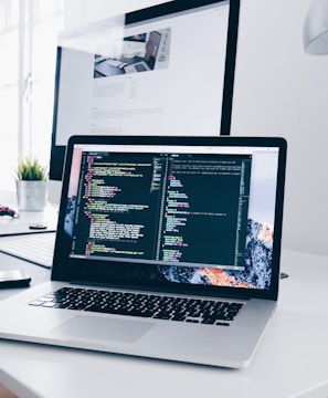 A MacBook with lines of code on its screen on a busy desk