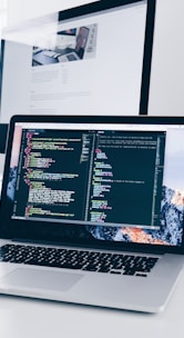 A MacBook with lines of code on its screen on a busy desk