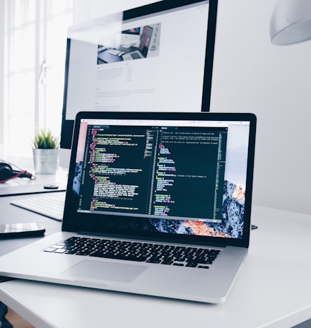 A MacBook with lines of code on its screen on a busy desk