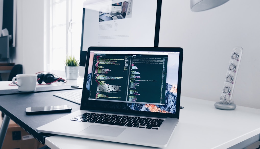 A MacBook with lines of code on its screen on a busy desk