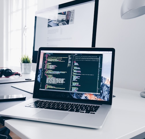 A MacBook with lines of code on its screen on a busy desk