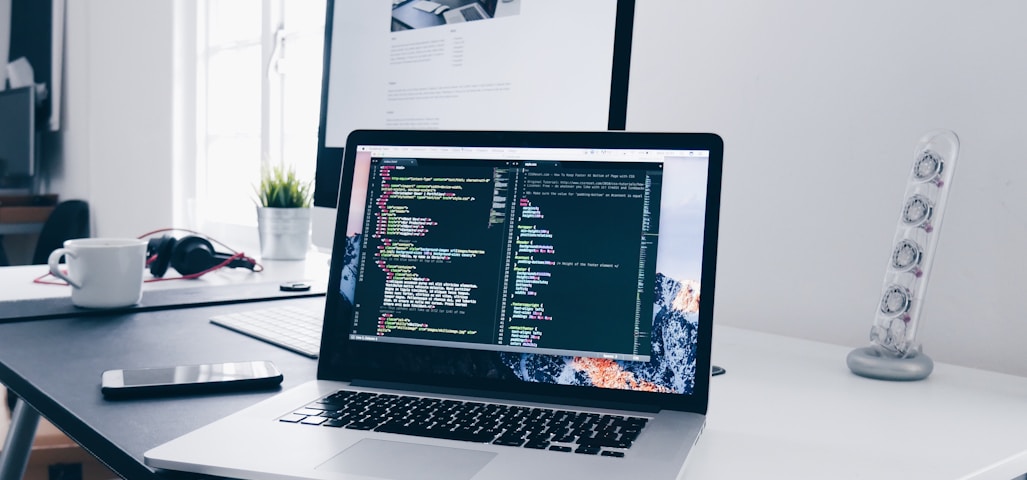 A MacBook with lines of code on its screen on a busy desk