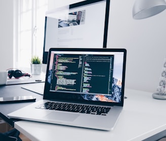 A MacBook with lines of code on its screen on a busy desk