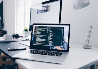 A MacBook with lines of code on its screen on a busy desk