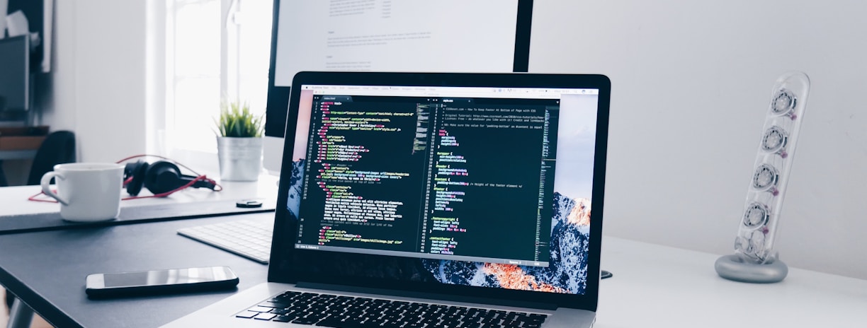 A MacBook with lines of code on its screen on a busy desk