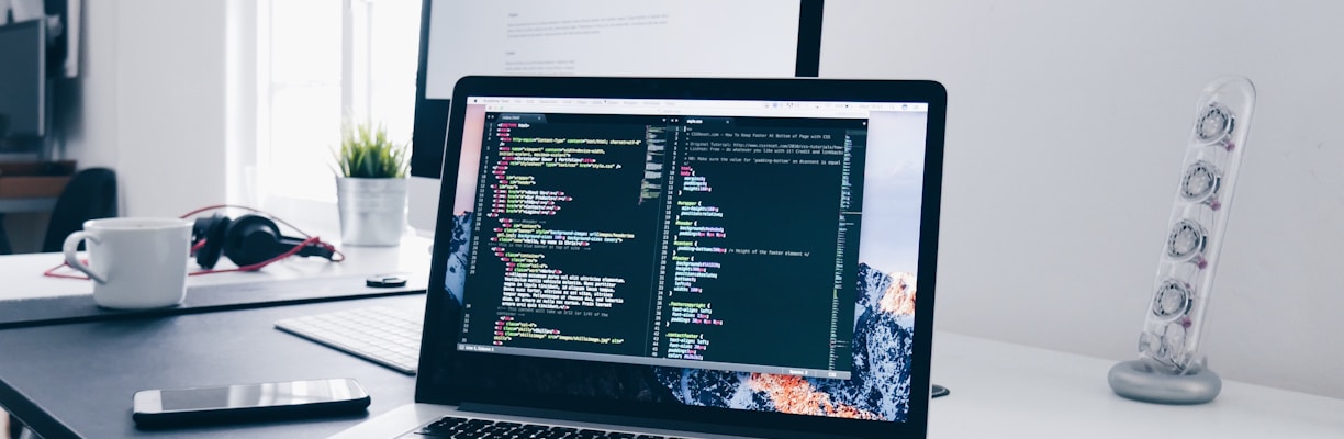 A MacBook with lines of code on its screen on a busy desk