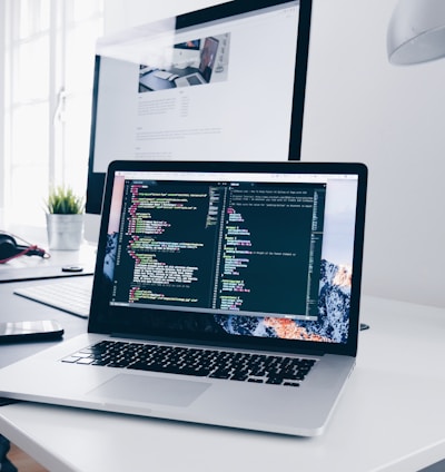 A MacBook with lines of code on its screen on a busy desk