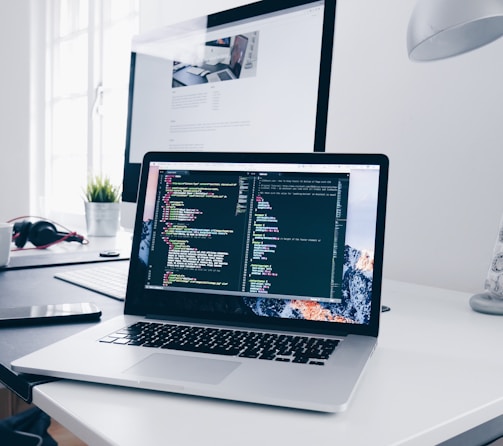 A MacBook with lines of code on its screen on a busy desk