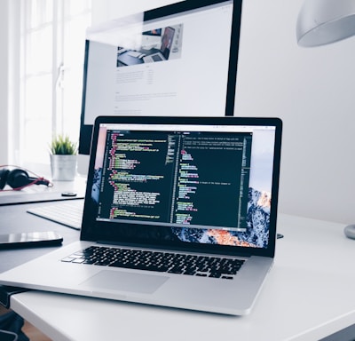 A MacBook with lines of code on its screen on a busy desk