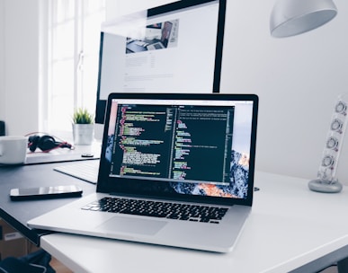 A MacBook with lines of code on its screen on a busy desk