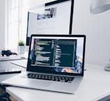 A MacBook with lines of code on its screen on a busy desk