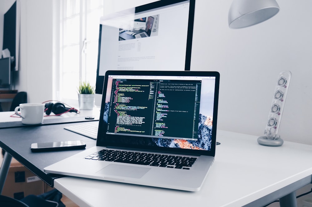 Un MacBook avec des lignes de code sur son écran sur un bureau occupé