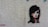 A stylized stencil painting of a woman's face with prominent black hair and red accents on a textured, light-colored wall. The artwork captures a mysterious and bold expression.