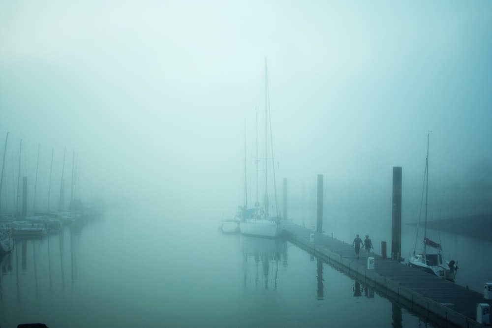 Dos personas que se desplazan a lo largo de la cubierta del muelle del barco de madera marrón por la niebla