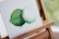 An abstract painting of two overlapping circular shapes with a textured finish, displayed on a wooden easel. The painting primarily uses shades of green and white, with visible brushstrokes creating a sense of depth.