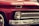 A close-up view of the front of a vintage red Chevrolet vehicle, featuring a classic design with prominent headlights, chrome detailing, and a visible license plate with the number FKKI03C. The paint is glossy, reflecting the surroundings, and the car's brand name is displayed on the grille.