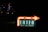 A brightly lit sign with an arrow pointing to the right, indicating 'ENTER' for valet or self parking. The sign is illuminated with white and red lights and is placed in a dark environment with city lights in the background.