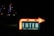 A brightly lit sign with an arrow pointing to the right, indicating 'ENTER' for valet or self parking. The sign is illuminated with white and red lights and is placed in a dark environment with city lights in the background.