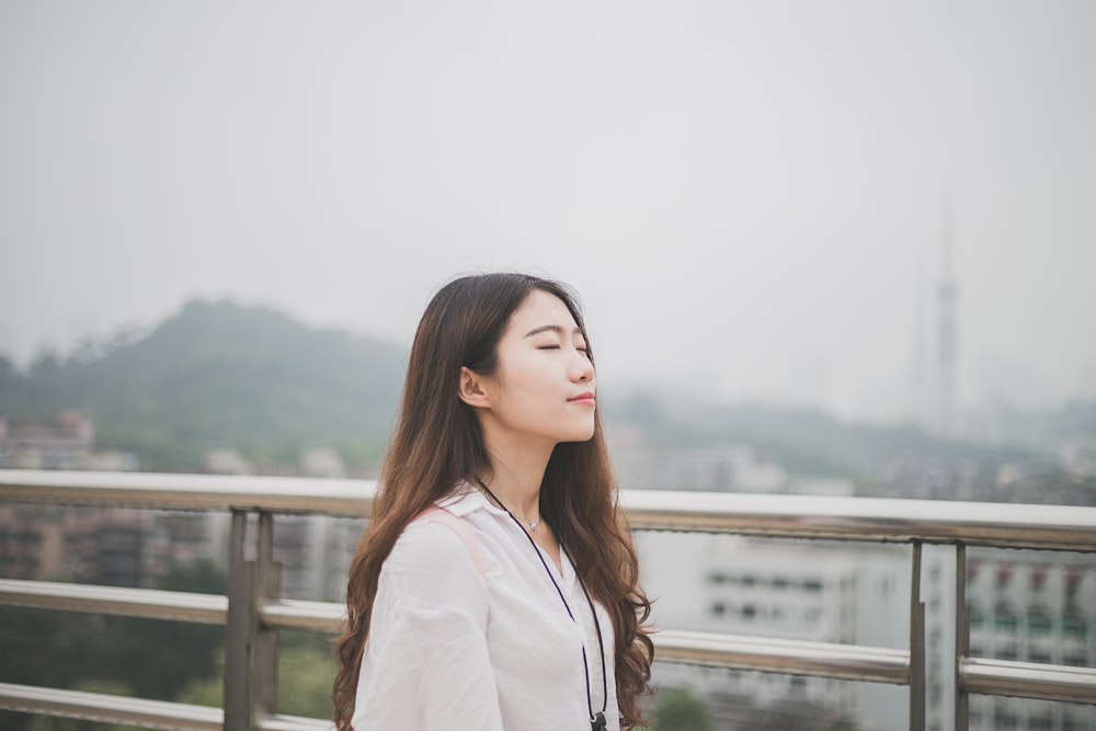 woman closing eyes white standing against stainless steel rail