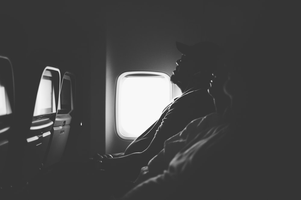 Photo en niveaux de gris de trois personnes assises à l’intérieur d’un avion