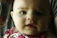 Close-up of a baby wearing a finely stitched, soft pastel-colored outfit.