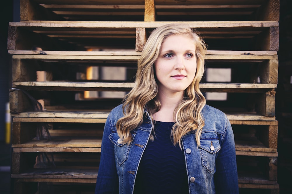 woman wearing blue button-up jacket besides brown wooden pallets