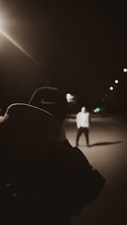 A candid shot of a mentor guiding a young person in a brightly colored hoodie under glowing streetlights.