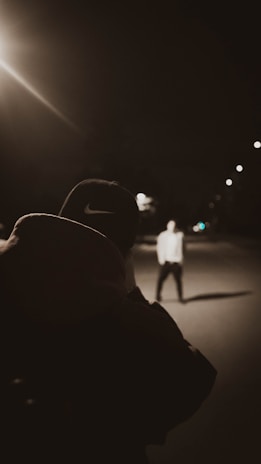A candid shot of a mentor guiding a young person in a brightly colored hoodie under glowing streetlights.