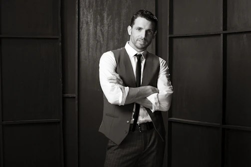 A sleek black-and-white photo of a confident man applying beard oil in a minimalist bathroom.