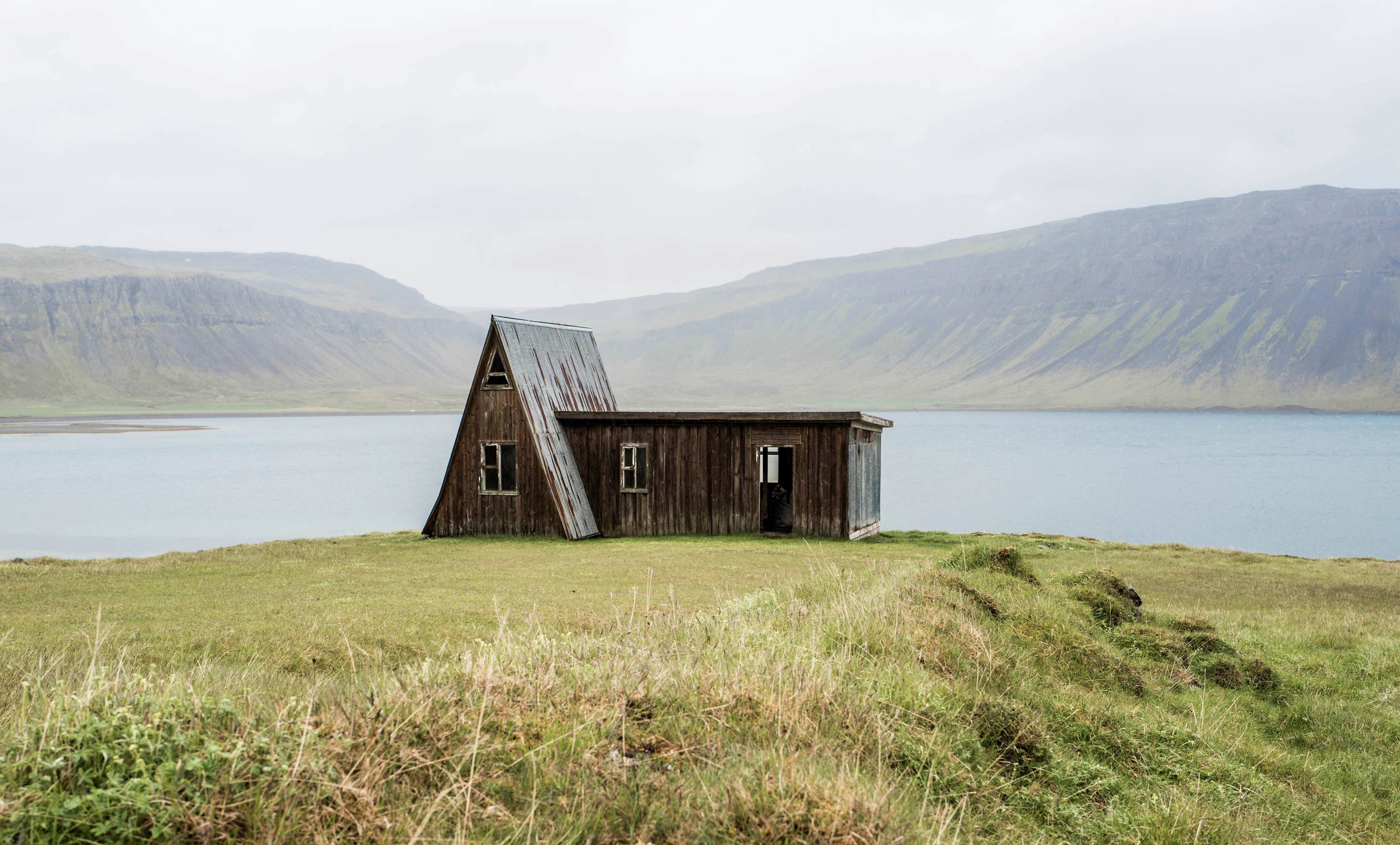 An old timber hut in long grass above a calm fjord in north-west Iceland