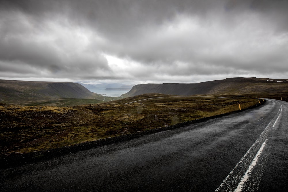 gray asphalt road near mountains under cloudy sky during daytime
