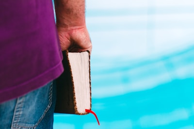 A thoughtful person reading a purple-covered book in a cozy study room.
