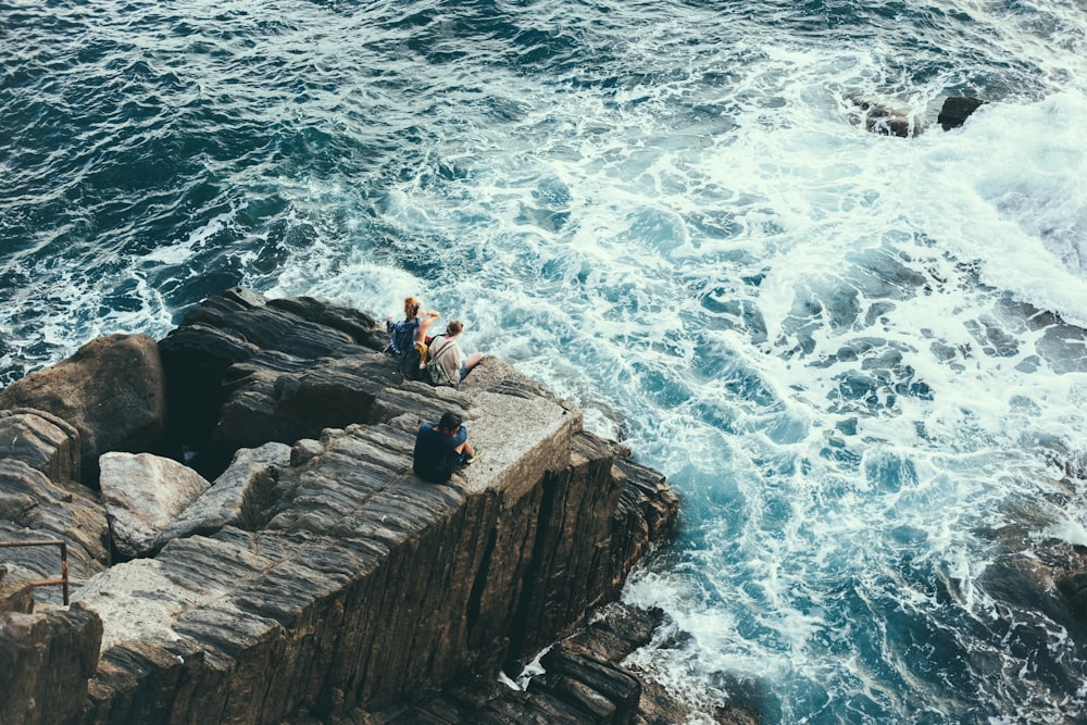 people sitting on rock formation on seashore