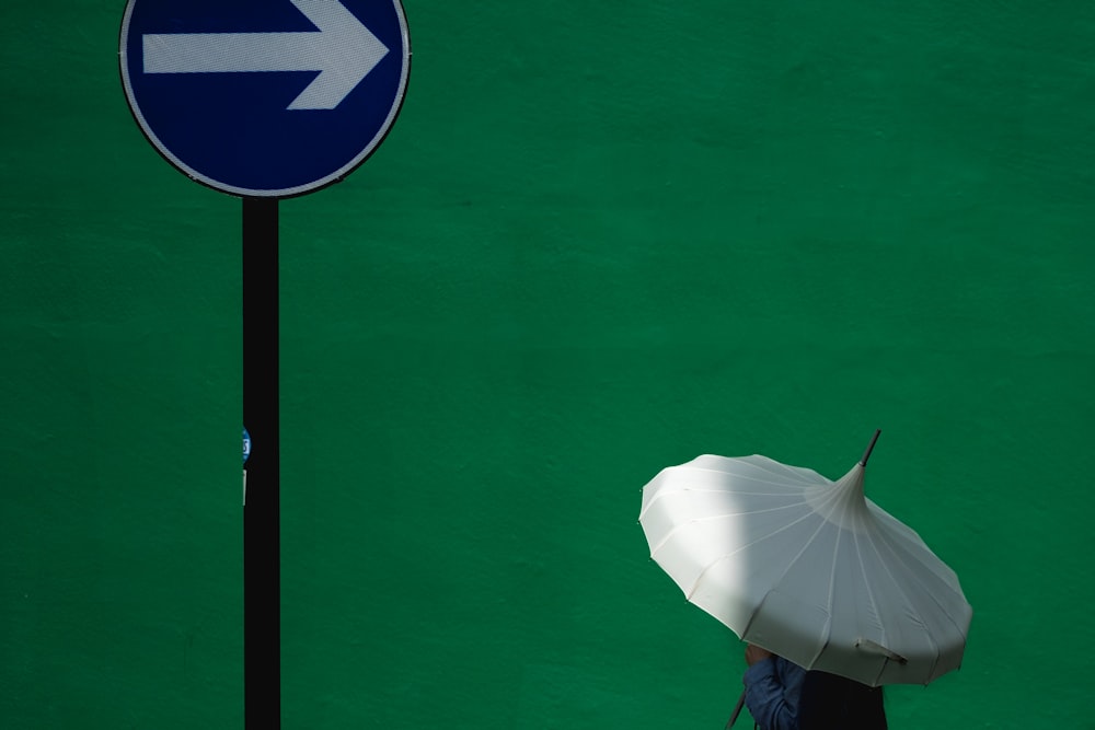 person using white umbrella near blue road signage