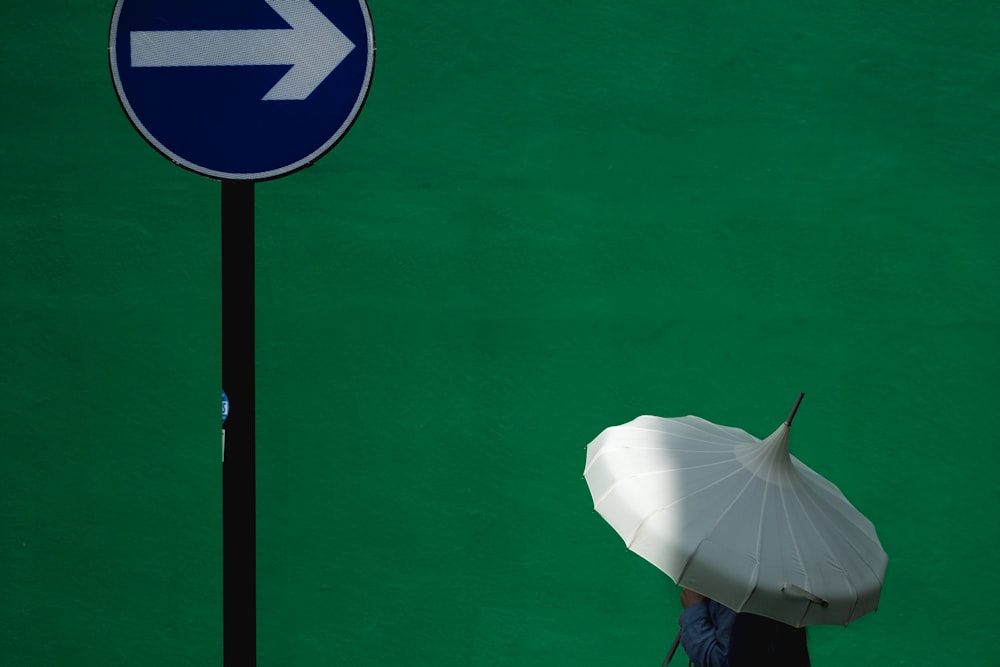 파란 도로 간판 근처에서 흰 우산을 사용하는 사람