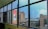 A view through large glass windows showcasing a cityscape with several multi-story buildings. One of the buildings prominently displays an LG advertisement. The sky is clear with a hint of clouds, adding to the urban environment captured from a higher floor with a wide-angle perspective.