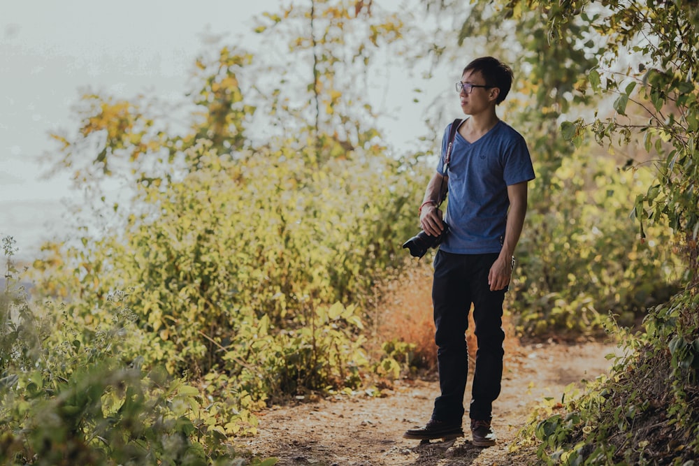 person wearing shirt standing on forest with DSLR camera